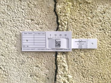 G1-Riss-Messlehre - Rissmonitor für innen und außen - mit QR-Code waagerecht über einem Riss montiert.