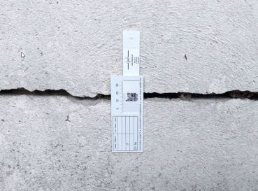 G1-Riss-Messlehre - Rissmonitor für innen und außen - mit QR-Code, senkrecht über einem Riss montiert.