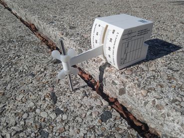 G3-Riss-Messlehre in frontaler Ansicht mit Skala zur Ablesung der Versatzhöhe sowie der Versatztaster, der auf einem tieferliegenden Natursteinbelag aufsitzt.