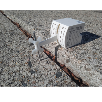 G3-Riss-Messlehre in frontaler Ansicht mit Skala zur Ablesung der Versatzhöhe sowie der Versatztaster, der auf einem tieferliegenden Natursteinbelag aufsitzt.