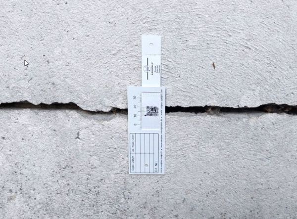 G1-Riss-Messlehre - Rissmonitor für innen und außen - mit QR-Code, senkrecht über einem Riss montiert.